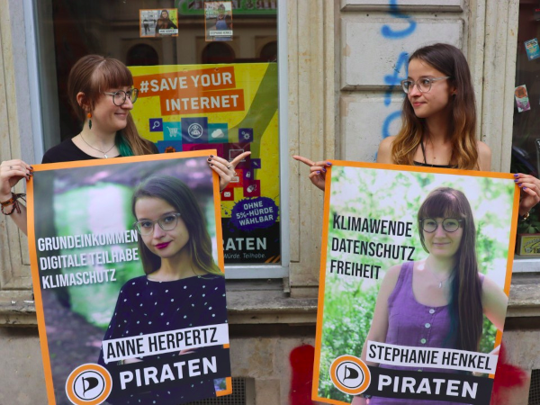 Anne und ich stehen nebeneinander, halten das Wahlplakat der jeweils anderen in der Hand, schauen uns an und zeigen dabei aufeinander Plakate Stephanie Henkel Anne Herpertz 2021 Piraten