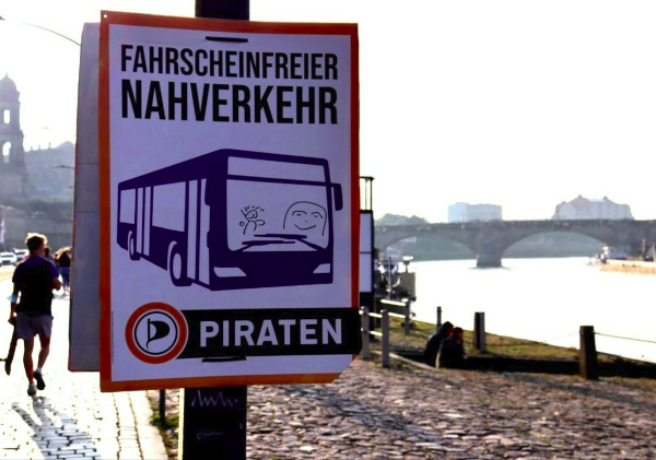Das Plakat Fahrscheinfreier ÖPNV an einer Laterne am Elb-Boulevard; Auf dem Plakat ist ein Bus zu sehen in den krakelige fröhliche Personen hineingemalt wurden Plakat Fahrscheinfrei Piraten